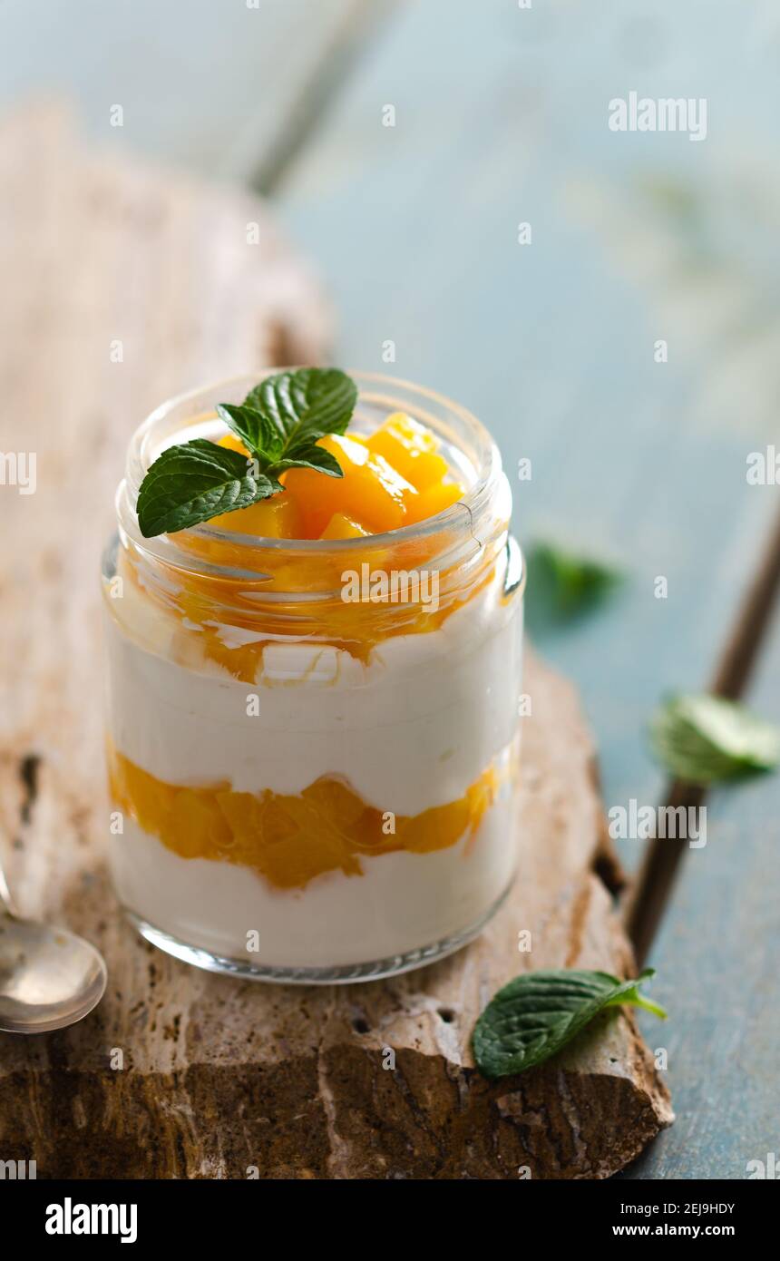 Einfacher Joghurt mit Pfirsich- und Minzblättern in einem Glas auf einem gelben Stein und hellblauer Holzkulisse. Stockfoto