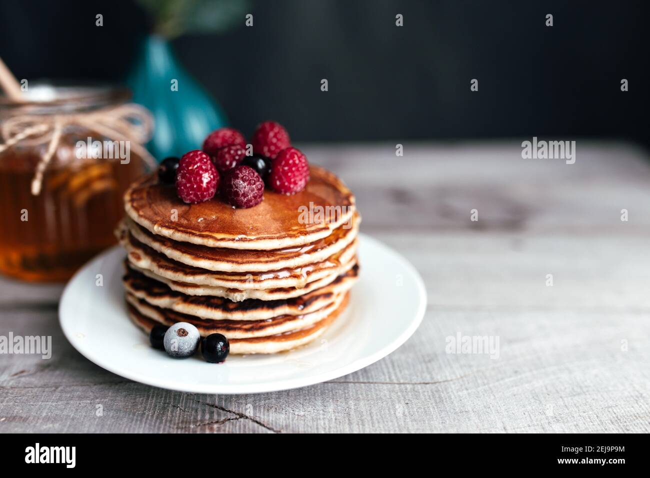 Saftige Pfannkuchen mit Beeren und Honig auf einem weißen Teller, Löffel, Glas, Holztisch. Hochwertige Fotos Stockfoto