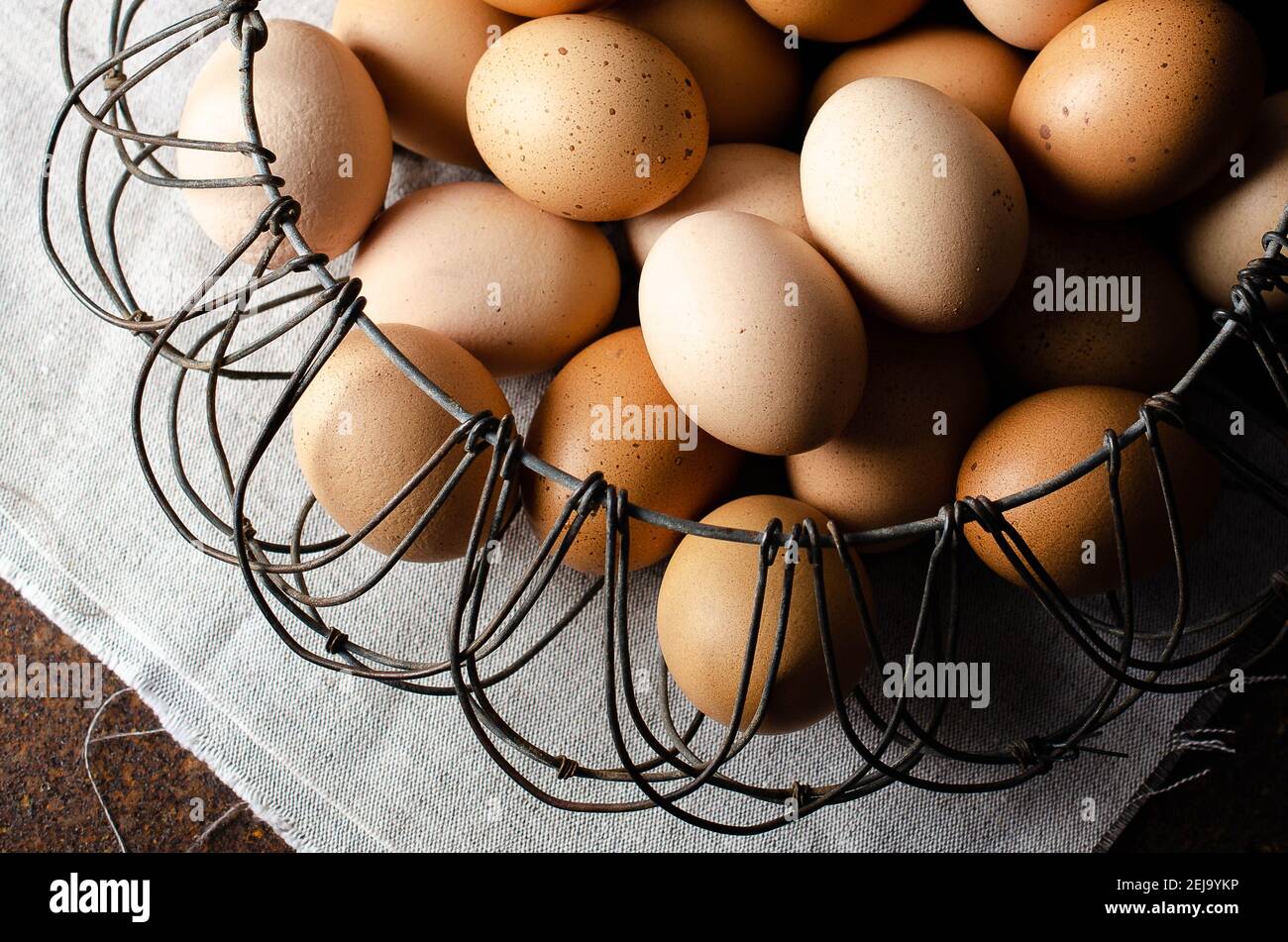 Eier in einem Wired-Korb auf einer beigen Serviette und dunklem Hintergrund. Stockfoto