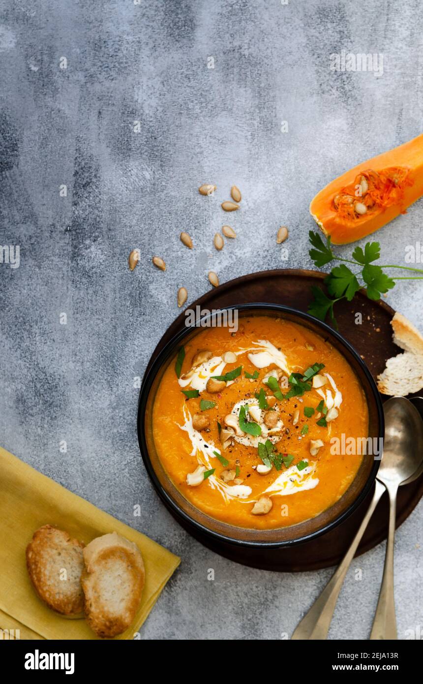 Butternut-Kürbissuppe mit Sahne, Cashew und Petersilie, in einer schwarzen Schüssel auf einem Holzteller. Stockfoto