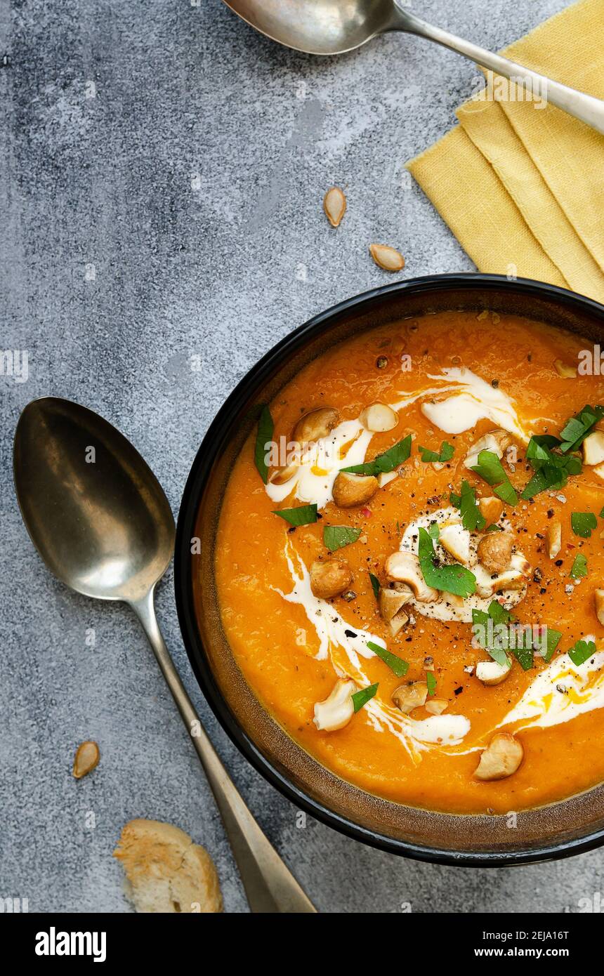 Butternut-Kürbissuppe mit Sahne, Cashew und Petersilie, in einer schwarzen Schüssel auf einem Holzteller. Stockfoto