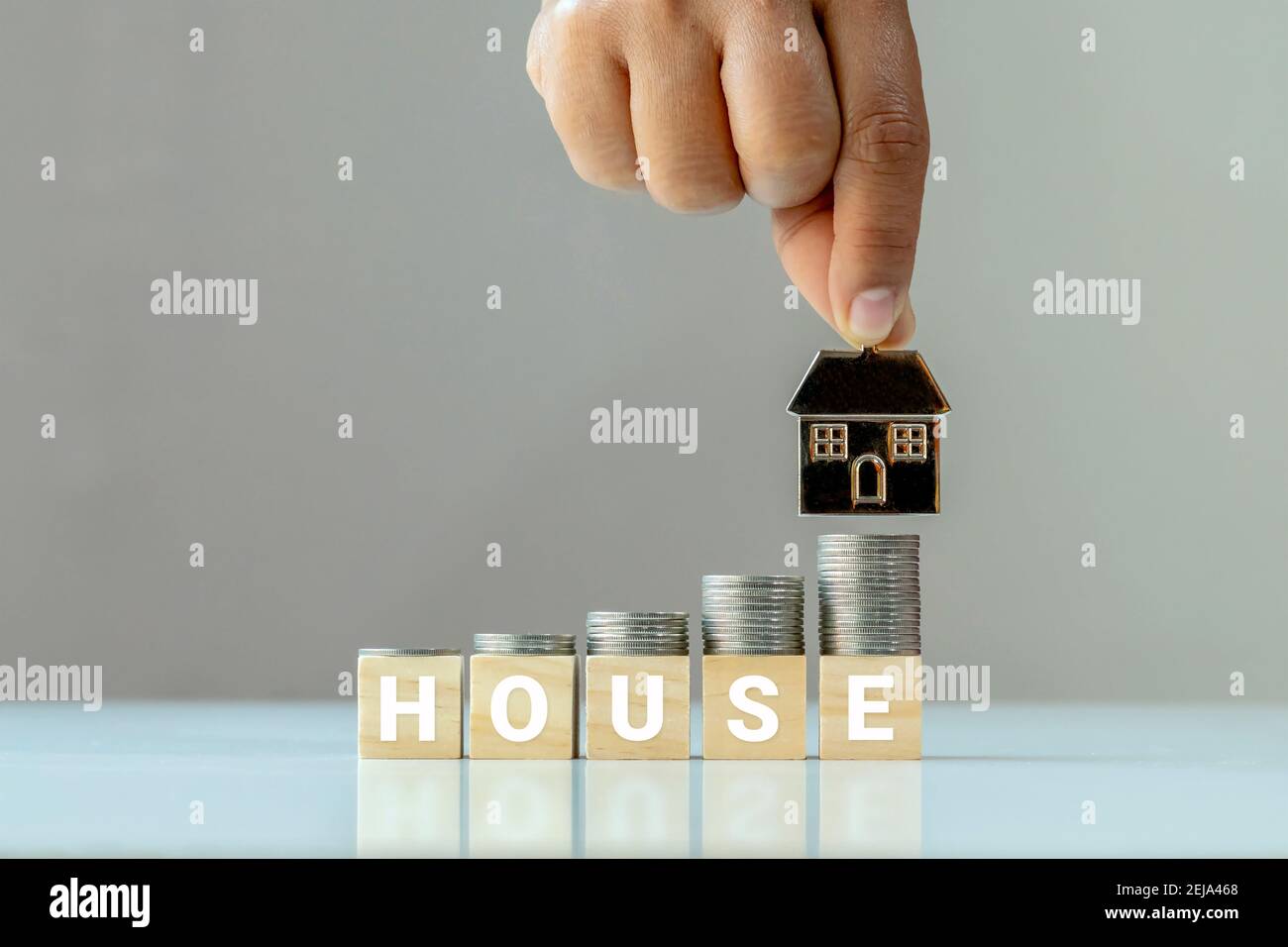 Die Stapel von Münzen sind auf dem Holzwürfel mit den Worten Haus und die Hand, die das Haus Modell. Finanz- und Investitionsideen über Real Stockfoto