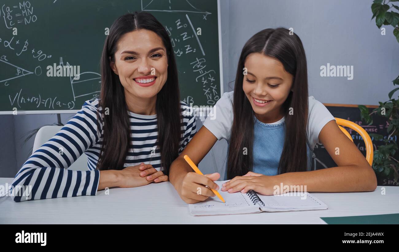 Mutter lächelt nahe glückliche Tochter, die Hausaufgaben zu Hause macht Stockfoto
