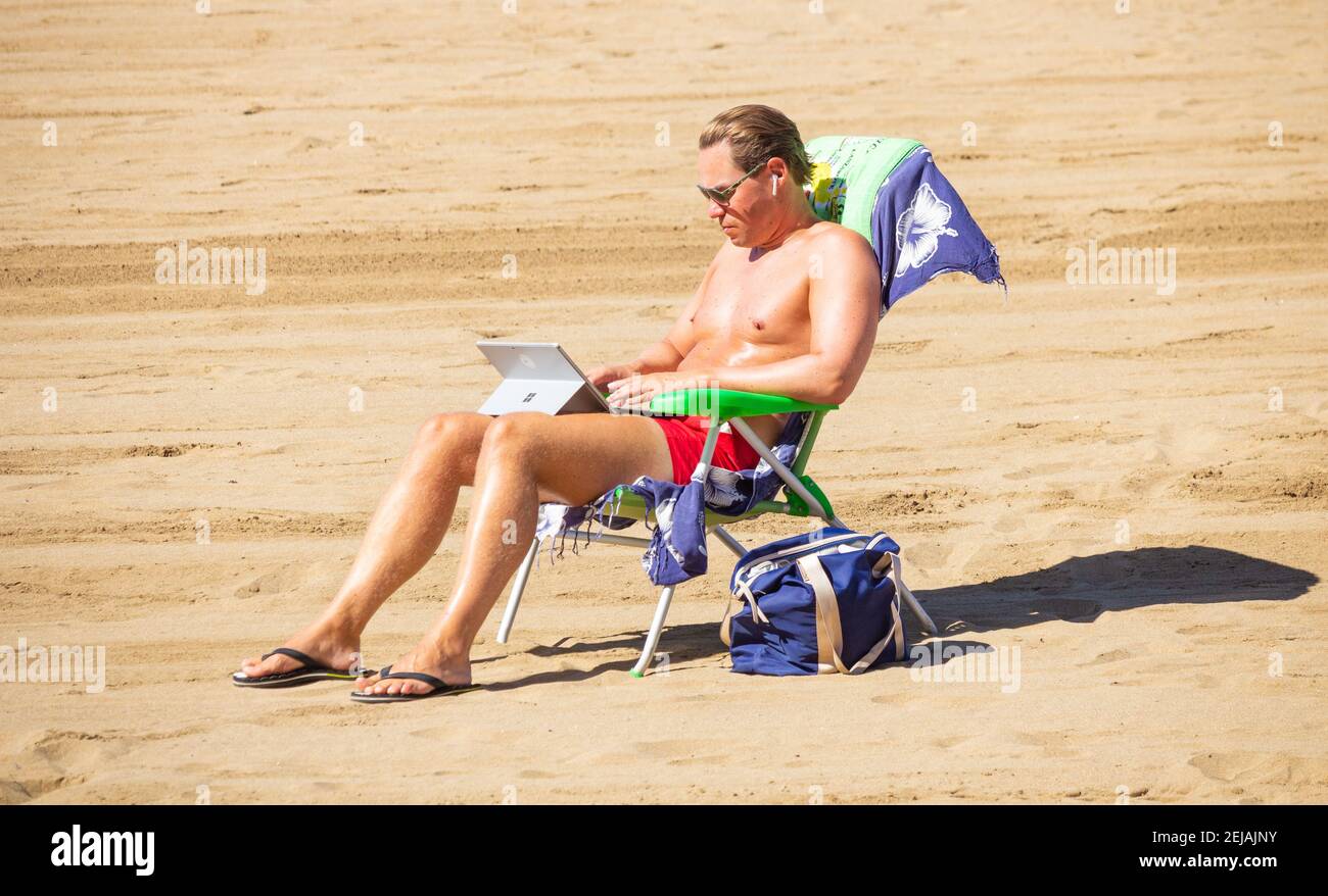 Mann, der am Strand in Spanien mit einem Laptop arbeitete. Stockfoto