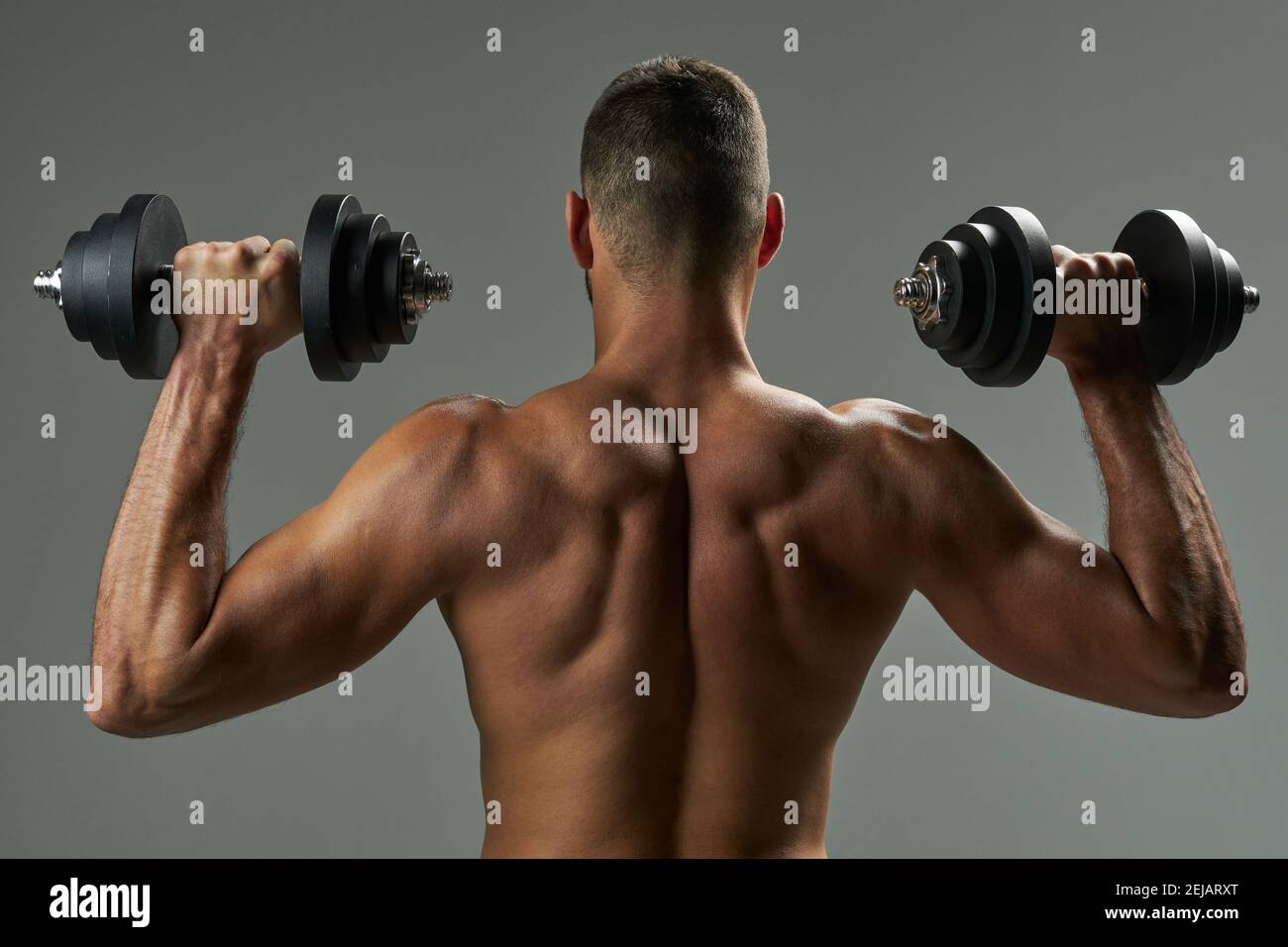 Taille nach oben Rückansicht Porträt von muskulösen Rücken und Hand Von unerkannten Sportler ganze halten Hanteln isoliert auf grauem Hintergrund Stockfoto