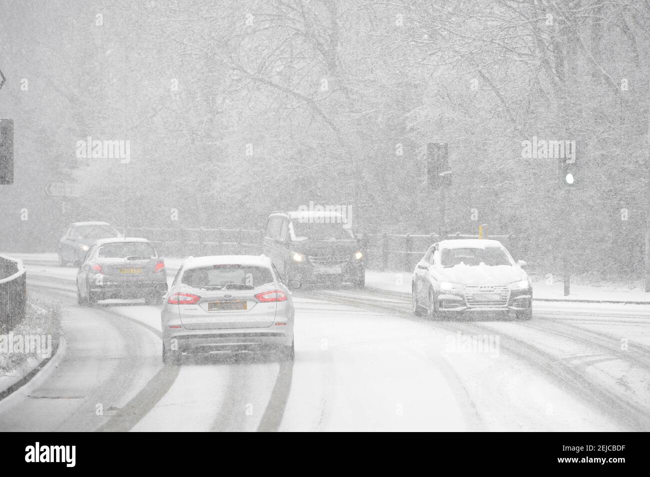 Autos fahren auf einer schneebedeckten Straße an einem Wintertag in Market Harborough, Leicestershire, Großbritannien. Stockfoto