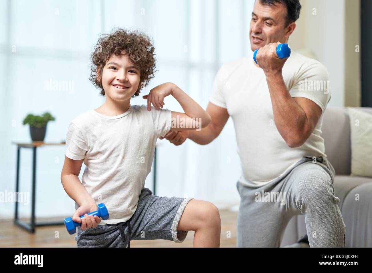 Kleine hispanische Junge Kind lächelt an der Kamera, während Training mit seinem Vater, Training mit Hanteln zu Hause. Aktiver Lebensstil, Elternschaft Konzept Stockfoto