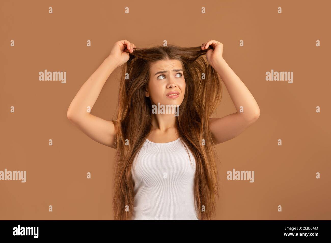 Was für eine Katastrophe. Verärgert junge Dame, die ihr verworrenes langes glattes Haar auf braunem Studiohintergrund anschaut Stockfoto
