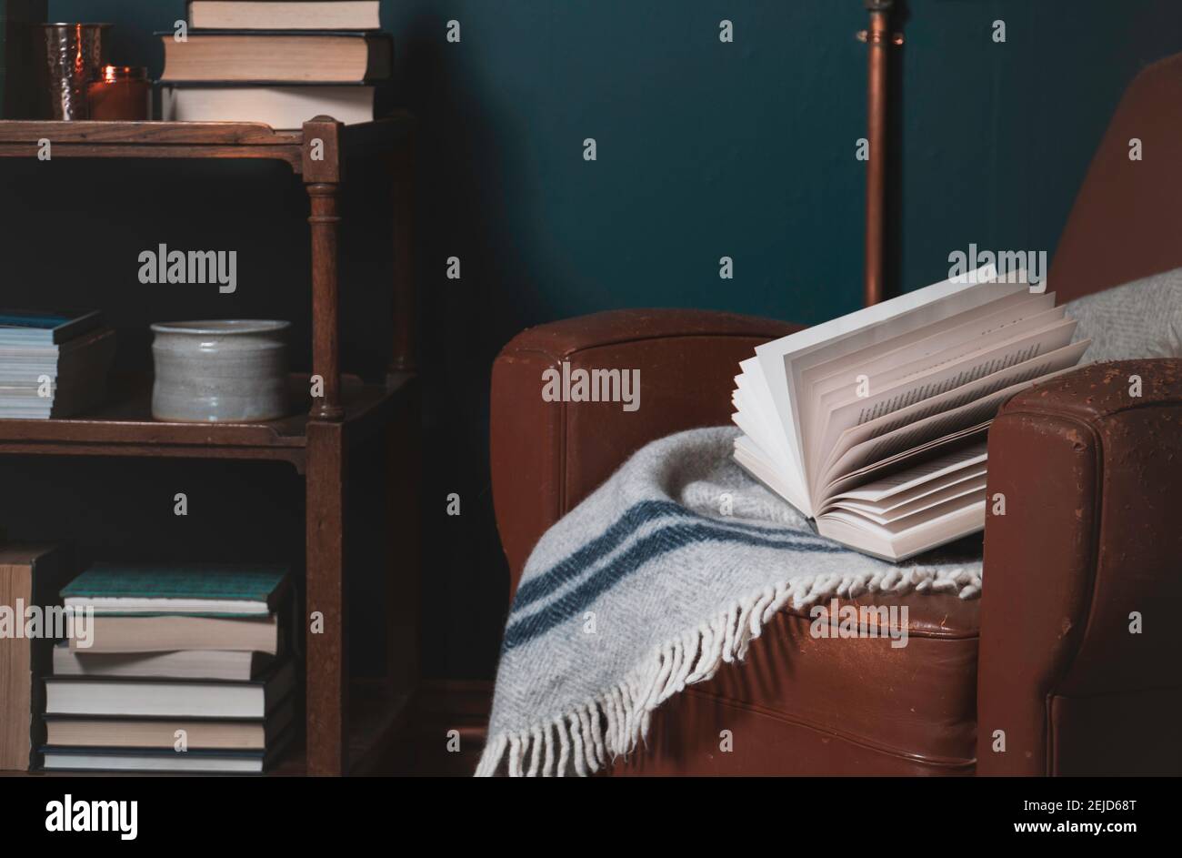 Landschaftsbild des Wohnraums. Ein Buch ruht auf einem alten Lederstuhl mit Büchern und Gegenständen, die im Hintergrund in Regalen zu sehen sind. Heimbüro, c Stockfoto