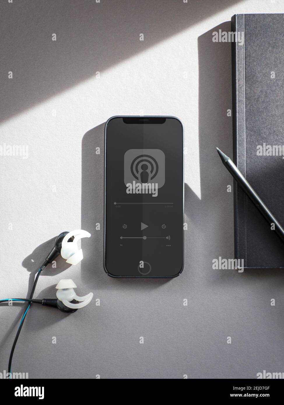 Schwarzes Telefon mit einem Podcast und ein Notebook und Kopfhörer daneben. Stockfoto