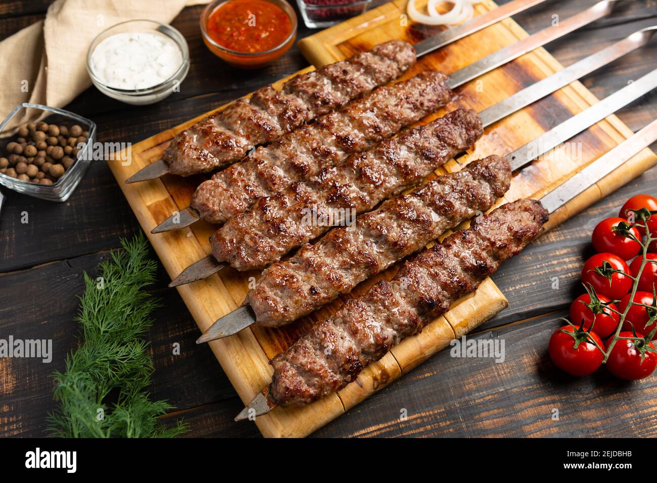 Kebab aus Hackfleisch auf Metallspieß mit Gemüse Und Sauce auf dunklem Holzhintergrund Stockfoto