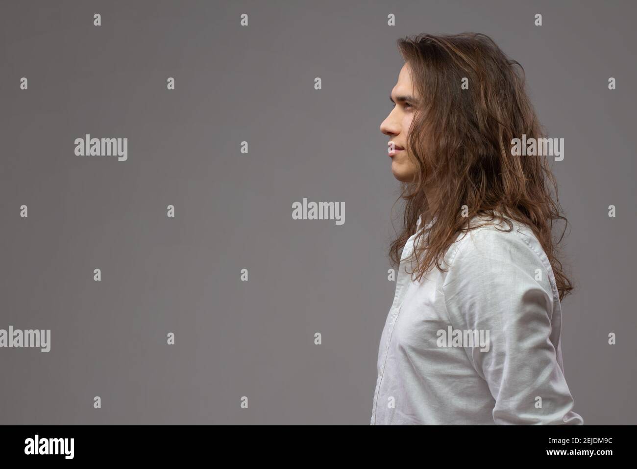 Profil des jungen Mannes mit langen Haaren im Studio. Attraktive Kerl in weißem Hemd isoliert auf grauem Hintergrund. Platz für Text kopieren Stockfoto