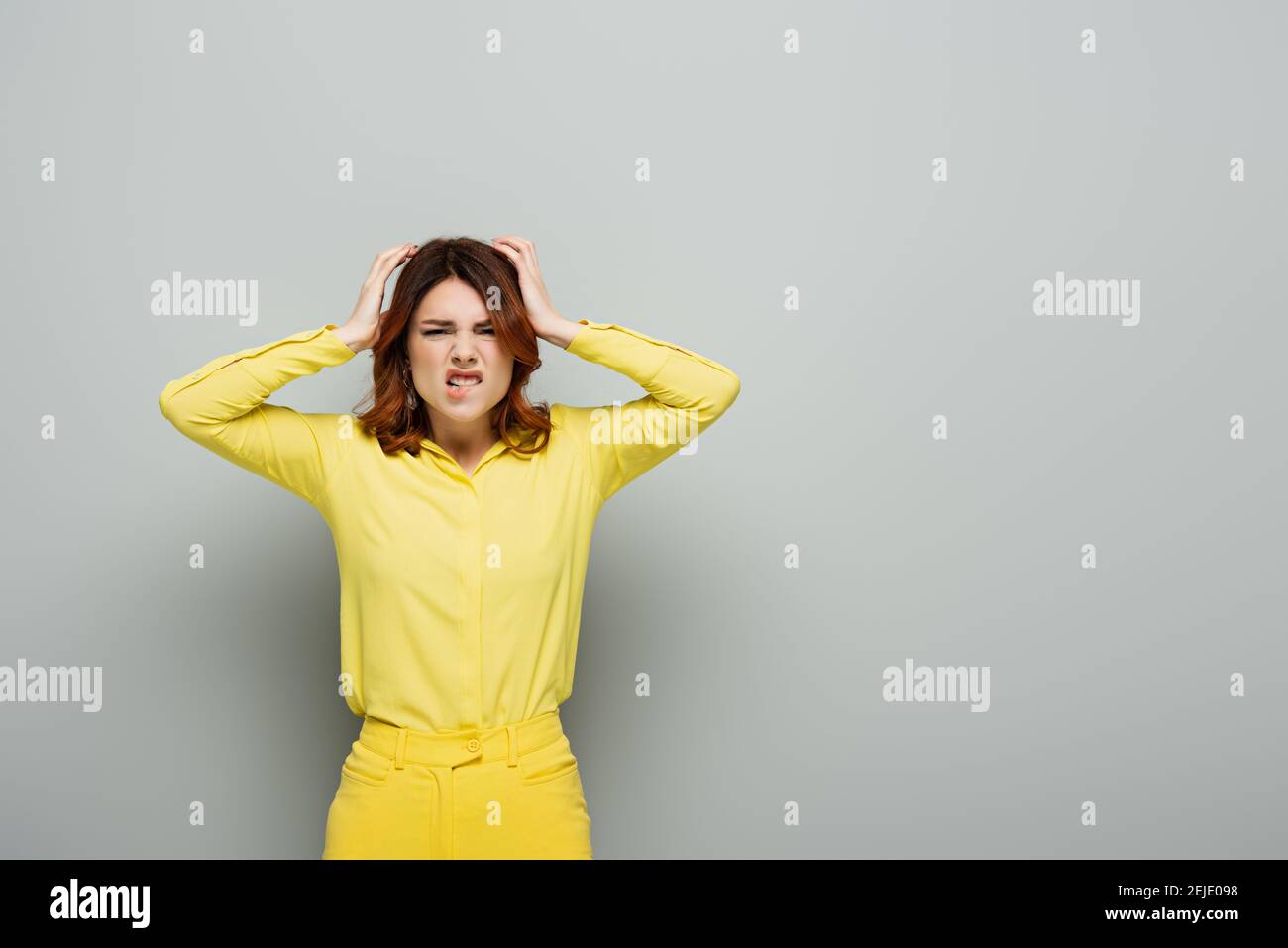 Unzufrieden Frau beißt Lippe und berühren Kopf auf grau Stockfoto