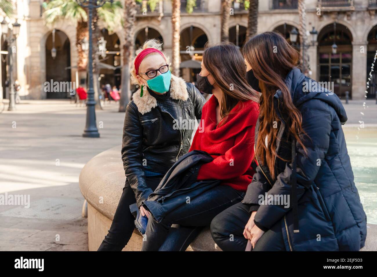 Drei weibliche Touristen in sonnigen mediterranen Stadt ruhen an einem Brunnen, tragen Schutzmaske. Konzept: Tourismus während der covid-19 Pandemie Stockfoto