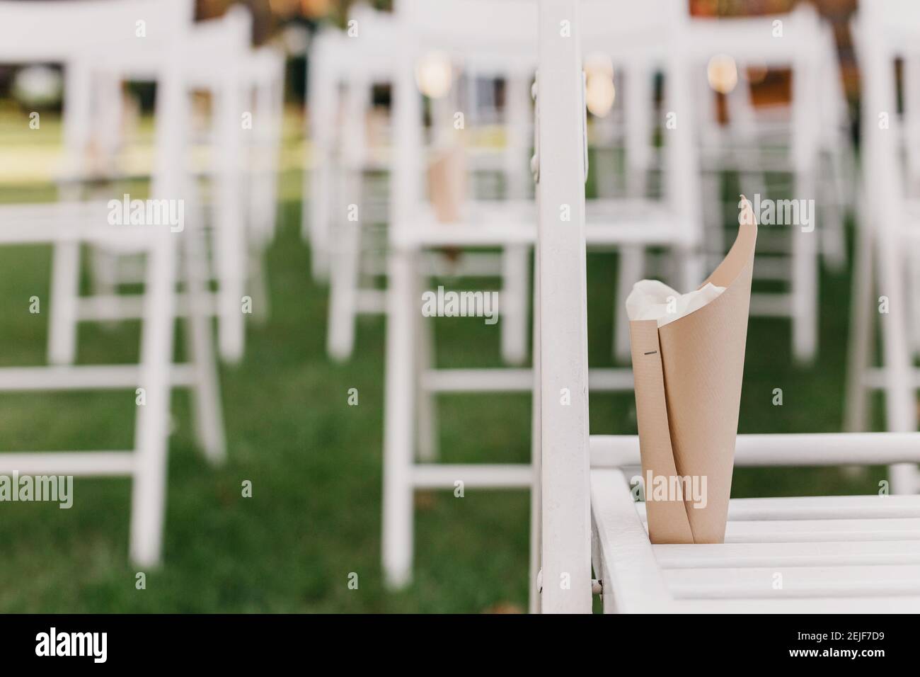 Weiße Klappstühle mit Papierpaketen mit Blütenblättern auf grün Rasen für Hochzeit im Freien Stockfoto