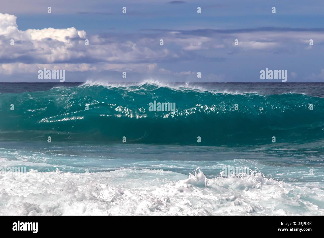 Wellen-Curling am hawaiianischen Strand. Spray fliegt zurück auf die Spitze der Welle. Schaumstoff aus früherer Welle im Vordergrund. Weißes Meeresspray in die Luft geworfen. Stockfoto