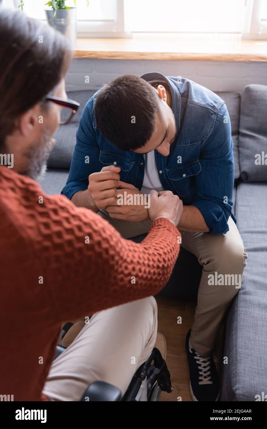 Behinderter Mann beruhigend frustriert hispanischen Sohn sitzt mit gesenktem Kopf, verschwommen Vordergrund Stockfoto