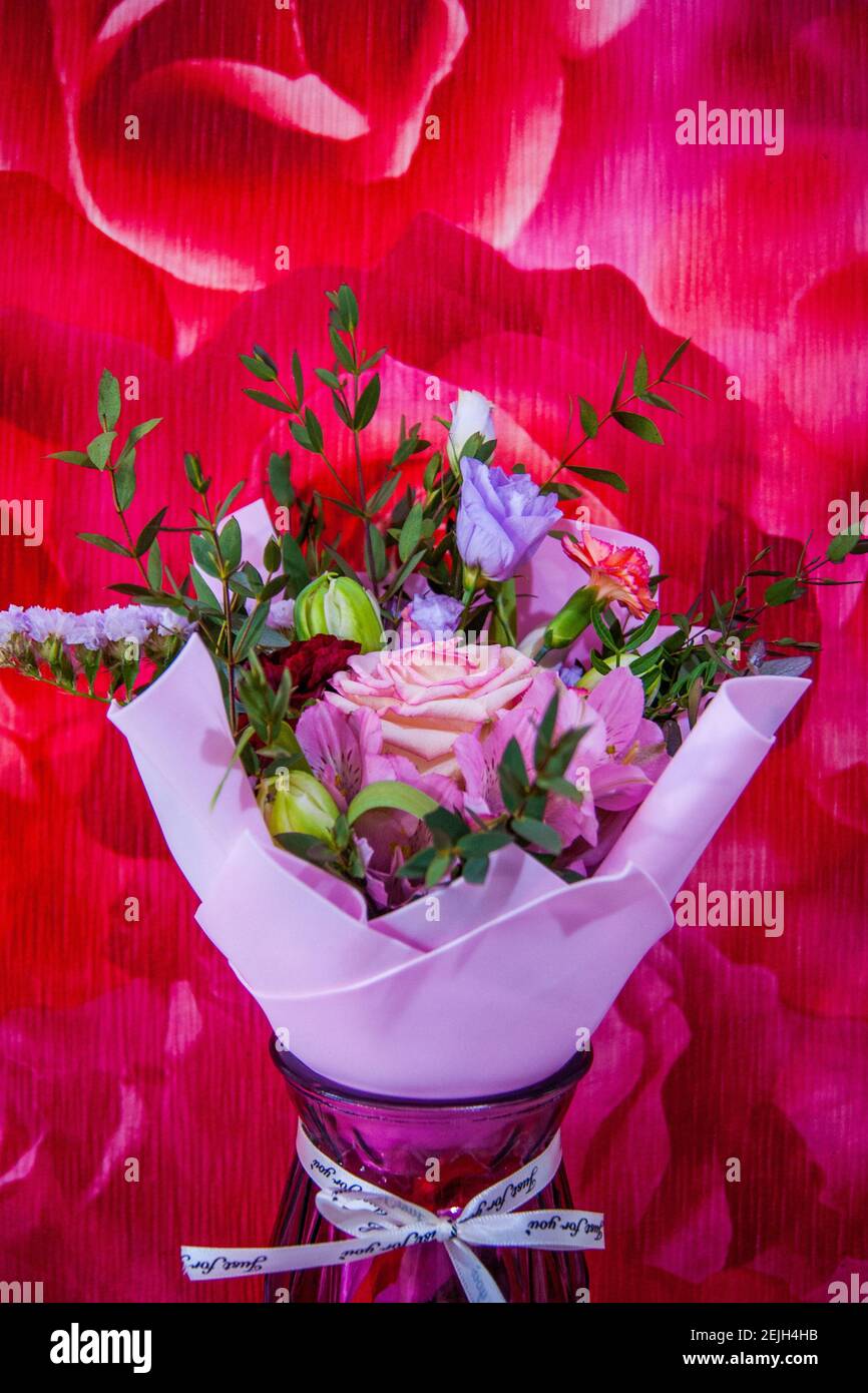 Ein zartes Blumenstrauß mit verschiedenen Blumen in einem hellrosa Wrapper steht in einer häuslichen Umgebung gegen eine bunte rosafarbene Wand. Vertikales Foto. Stockfoto