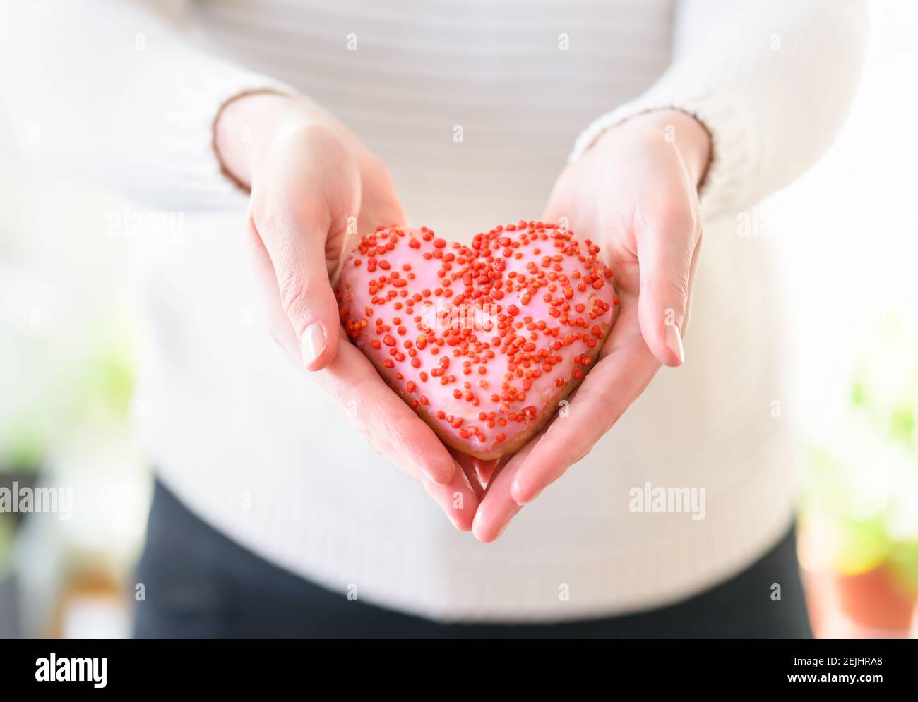 Herz in der Hand, Valentinstag Konzept Foto mit einem leckeren Herz Donut Stockfoto