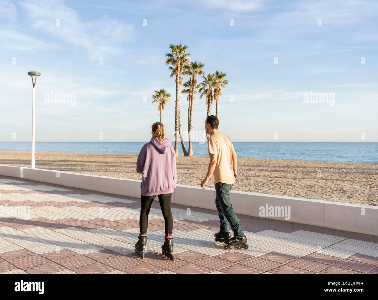 Junges Paar Rollschuhlaufen in Promenade am Meer mit Palmen im Hintergrund.Rückansicht von Sport und Fitness Lifestyle Konzept mit Kopierraum Stockfoto