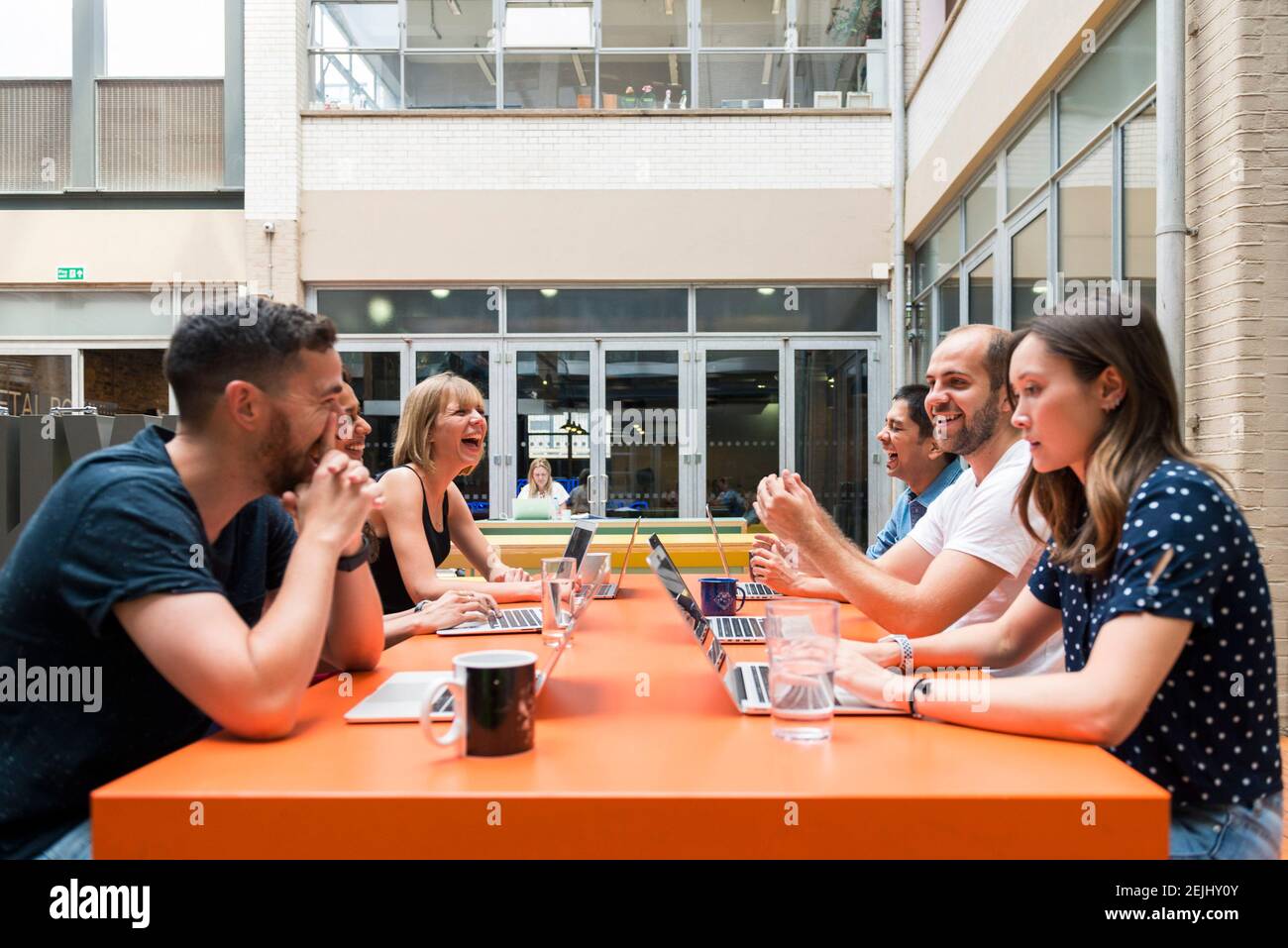 Sechs Mitarbeiter sitzen in einem modernen und hellen Büro an einem offenen Besprechungstisch in einem Gemeinschaftsraum und treffen sich produktiv Stockfoto