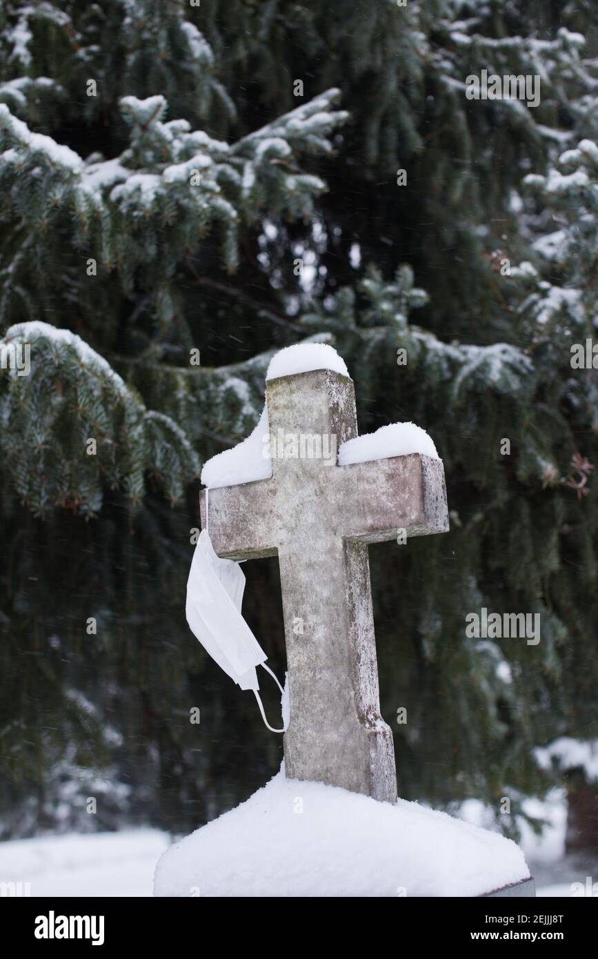 Covid 19 Tod. Eine Gesichtsmaske, die auf dem Kreuz in einem Friedhof hängt, Friedhof. Coronavirus-Opfer. Pandemie der nordischen Länder. Wie kann man Coronavirus verhindern? Stockfoto