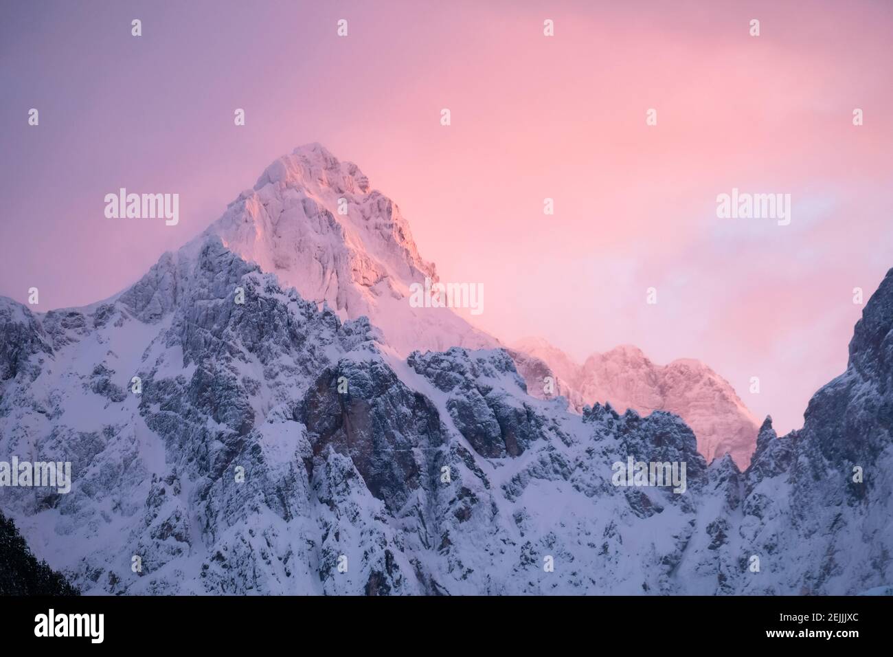 Wunderschöne Nahaufnahme eines rosa glühenden Berggipfeln in den Alpen bei Sonnenuntergang, während der Wind Schnee vom Berg weht. Kraft natürlicher Elemente Stockfoto