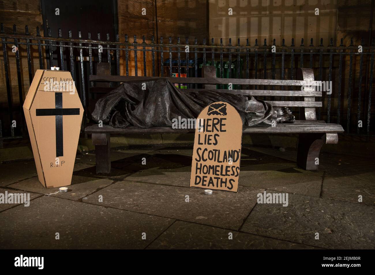 Glasgow, Schottland, Großbritannien. Februar 2021, 22nd. Im Bild: Eine Skulptur eines Obdachlosen, der auf einer Parkbank schläft, mit einem grabsteinförmigen Plakat, auf dem steht: „HIER LIEGEN OBDACHLOSE IN SCHOTTLAND“. Heute, am 23rd. Februar 21, hat die schottische Regierung die Zahl der Obdachlosen-Todesfälle 3 Tage früher freigegeben, die um 11% höher sind als im letzten Jahr. Der Link https://www.nrscotland.gov.uk/news/2021/homeless-deaths-2019 zeigt den Artikel heute. Quelle: Colin Fisher/Alamy Live News Stockfoto