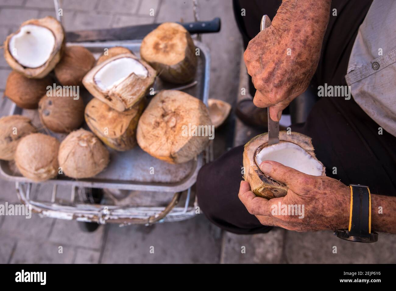 Alte Männerhände schneiden Kokosfleisch aus Kokosnuss mit Messer. Stockfoto