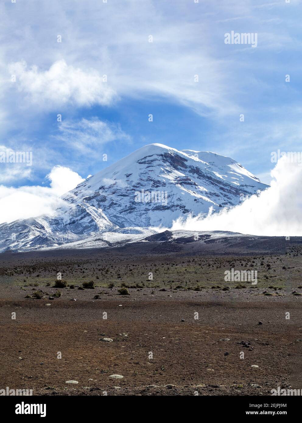 Vertikale Aufnahme des Vulkans Chimborazo, umgeben von Wolken in einem blauen Himmel. Reisen Sie in Ecuador in den Anden Südamerikas. Stockfoto