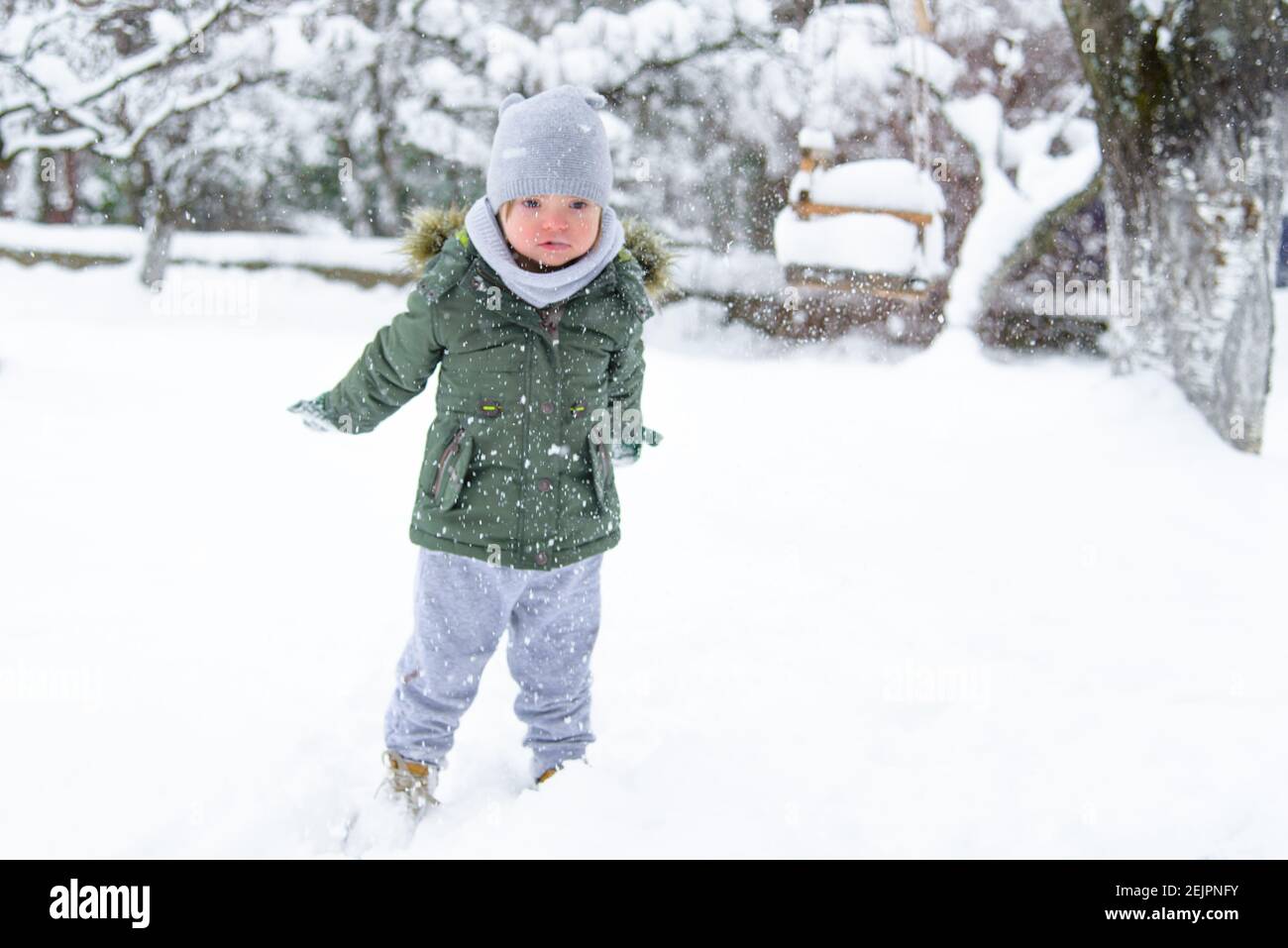 Down-Syndrom Kleinkind Junge wirft Schneeflocken aus seinen Händen. Verschwommen. Behinderter Junge genießt das frostige Winterwetter und Schnee. Winterspaß im Hof. F Stockfoto
