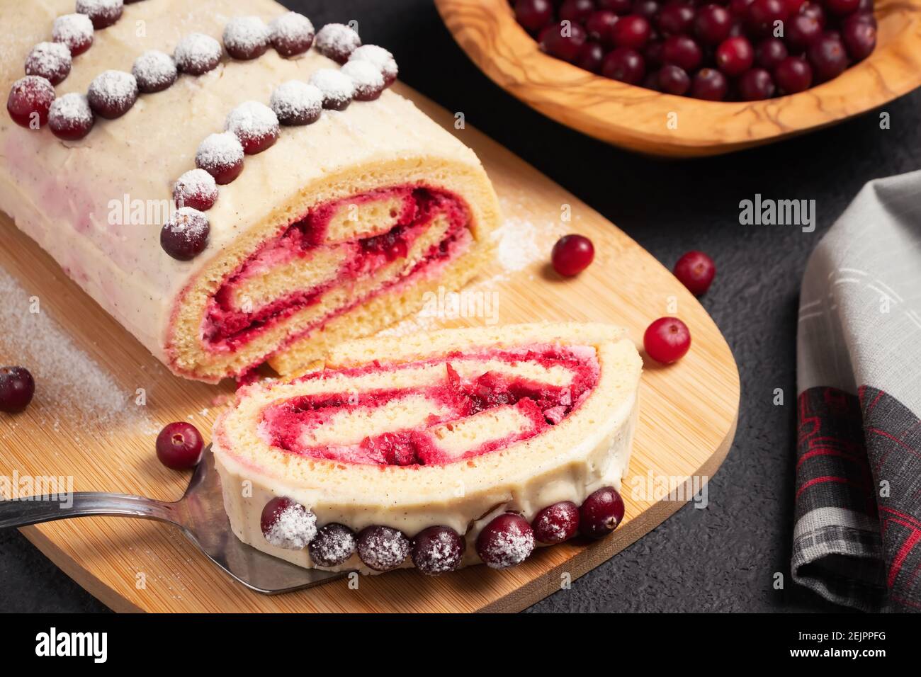 Hausgemachte Biskuit süße Rolle mit Preiselbeeren und Sahne auf einem schwarzen Tisch. Stockfoto