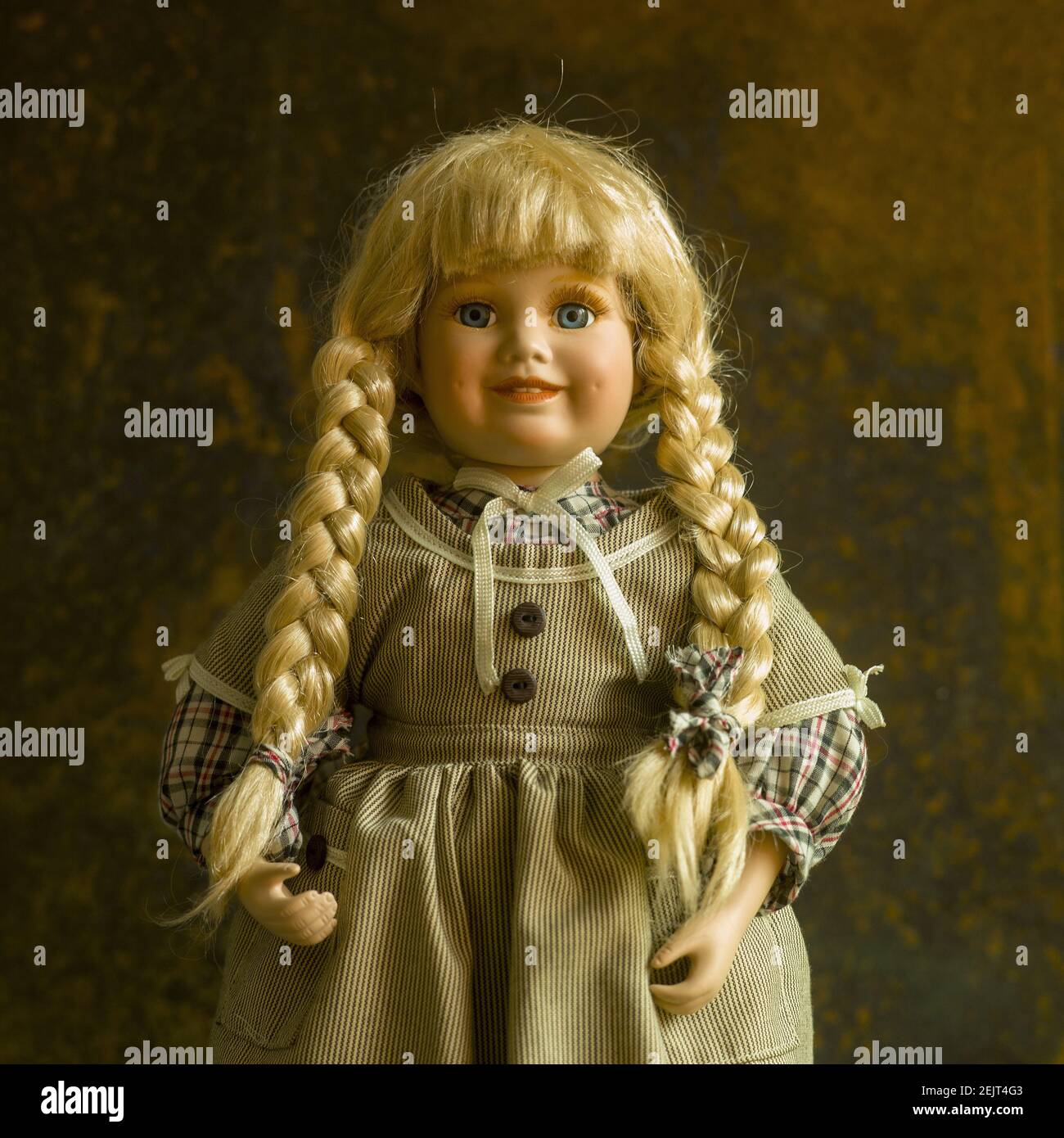 Vintage Puppe mit einem schönen Kleid und goldenen Zöpfen an Der braune Hintergrund Stockfoto