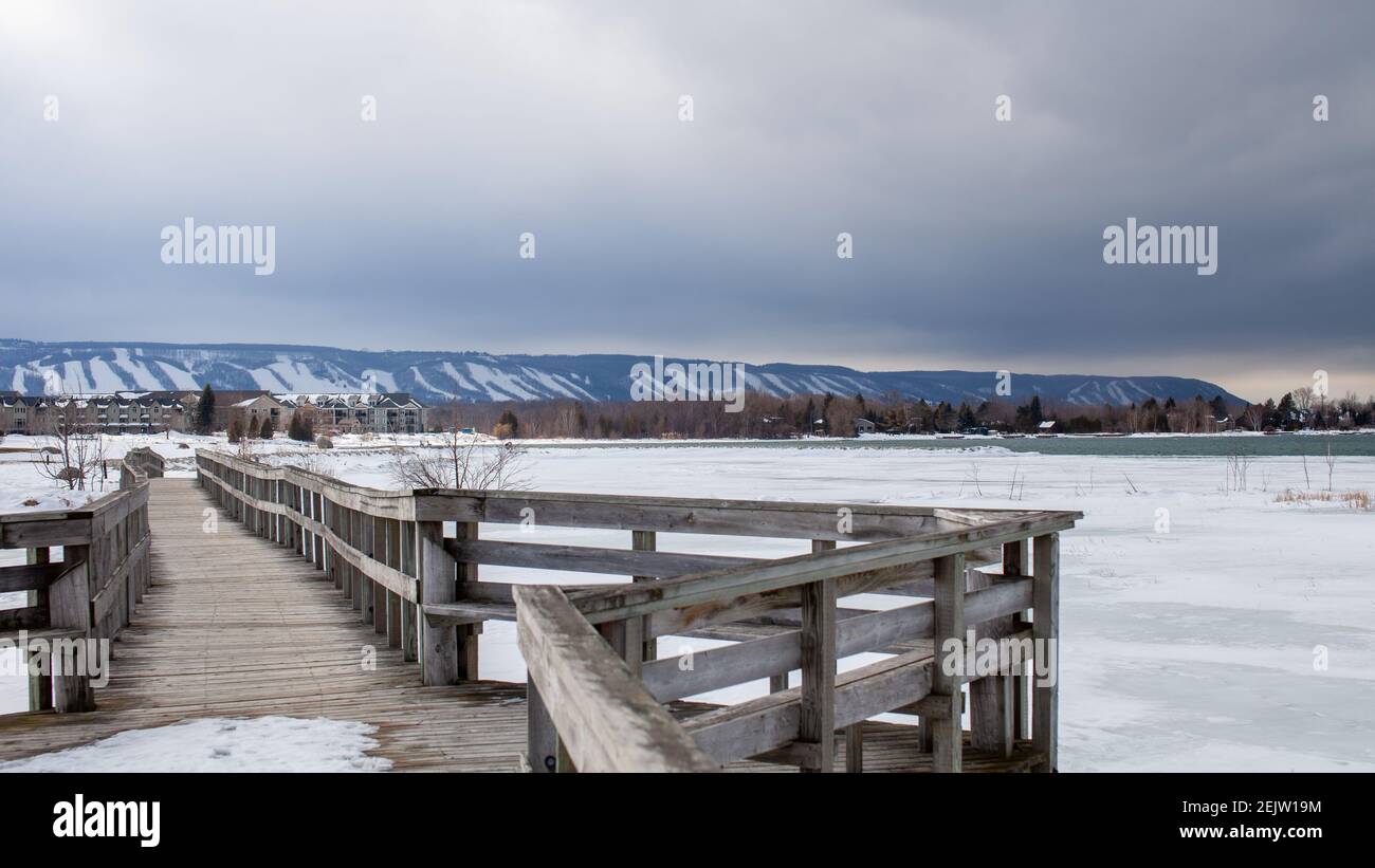 Eine Holzbrücke in Lighthouse Point, Collingwood, durchquert einen Teil der Georgian Bay und überblickt die Blue Mountain Ski Hills aus der Ferne Stockfoto