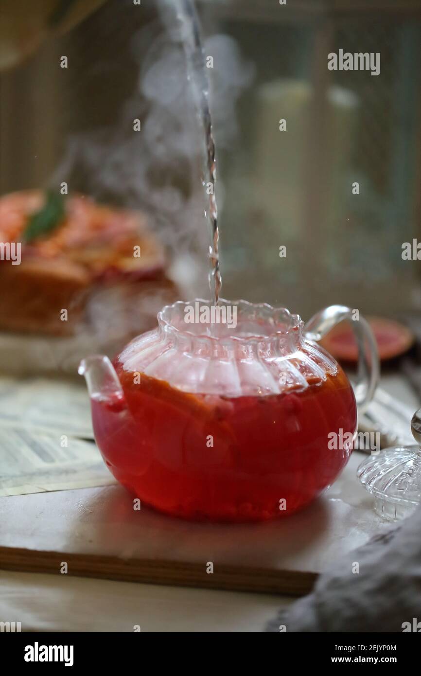 Kochendes Wasser wird in eine Glas-Teekanne mit Preiselbeeren gegossen  Stockfotografie - Alamy