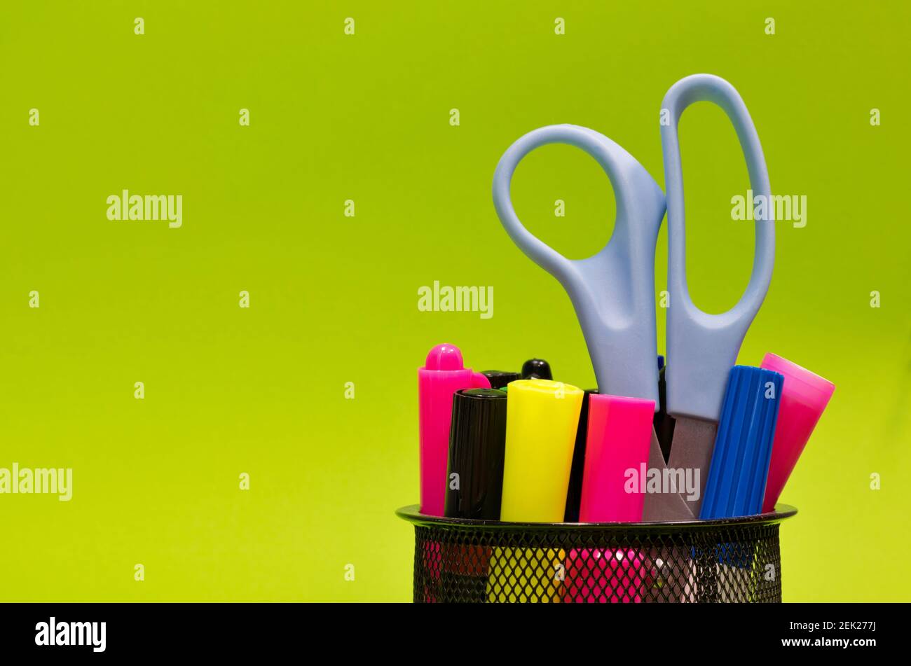 Mesh-Stiftbecher voll mit bunten Markern, Schreibutensilien und Scheren auf einem schlichten grünen Hintergrund mit Kopierraum, Konzeptbild. Stockfoto