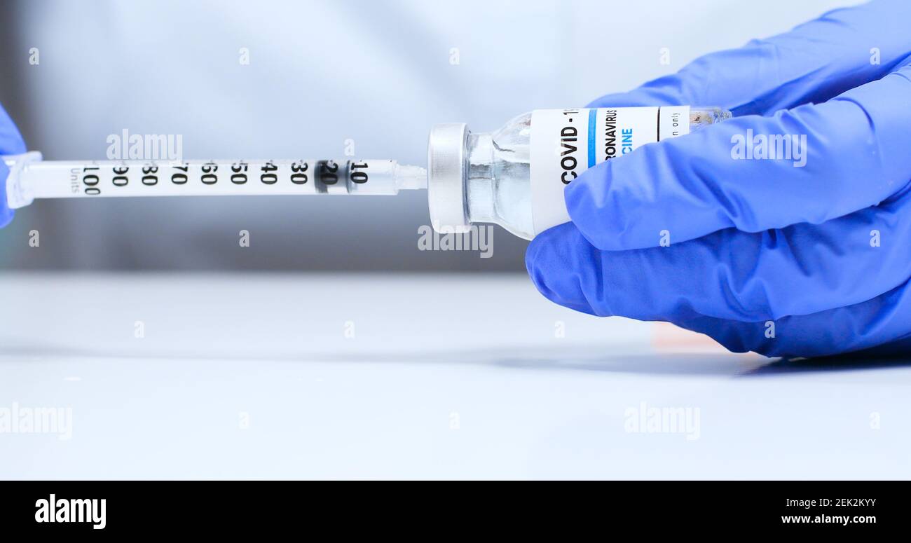 Nahaufnahme der weiblichen Hände in blauen medizinischen Handschuhen mit durchsichtiger flüssiger Coronavirus SARS-Cov-2 Impfstoffflasche und Spritze zur Injektion im Labor. Forschung und Entwicklung neuer Heilmittel für Krankheiten Stockfoto