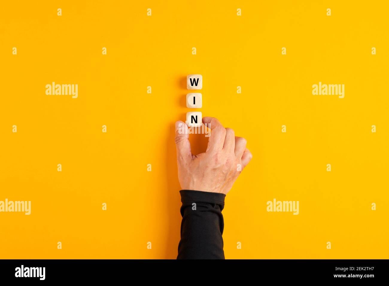 Männliche Hand, die die Holzblöcke mit dem Wort gewinnen auf gelbem Hintergrund. Erfolgsstrategie im Geschäfts- oder Wettbewerbskonzept. Stockfoto