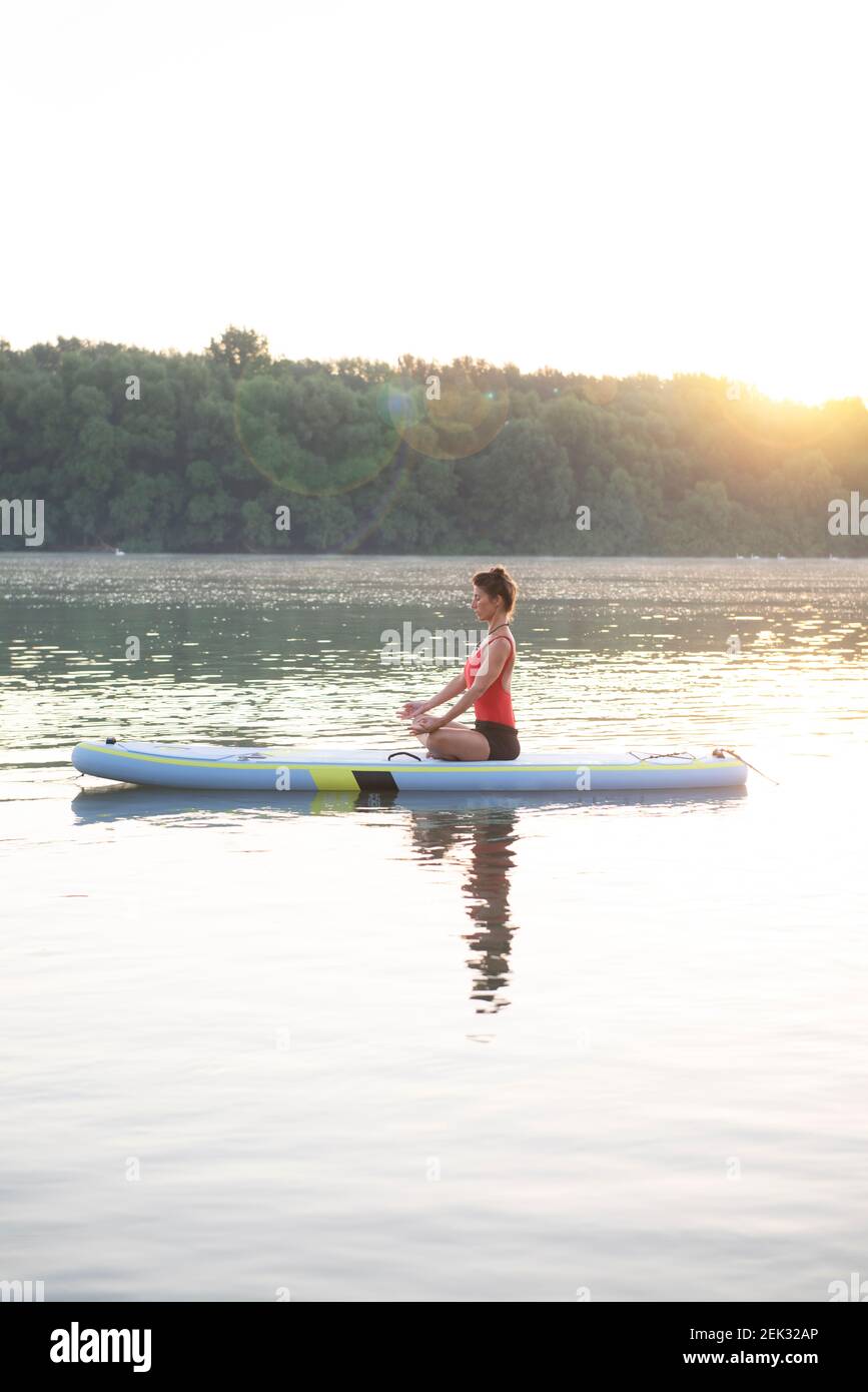 Frau meditiert und praktiziert Yoga während des Sonnenaufgangs auf einem Paddleboard Stockfoto