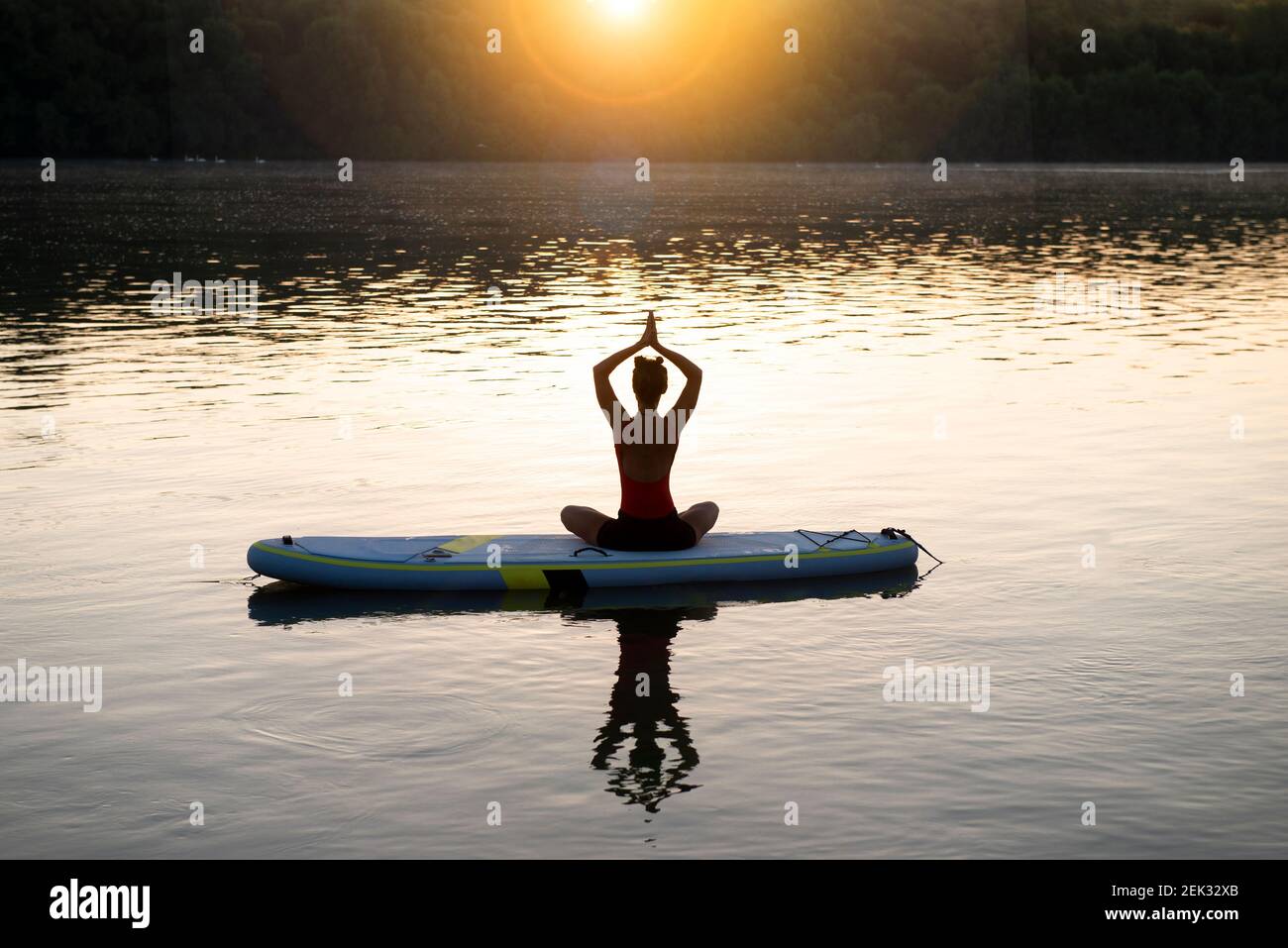 Frau meditiert und praktiziert Yoga während des Sonnenaufgangs auf einem Paddleboard Stockfoto