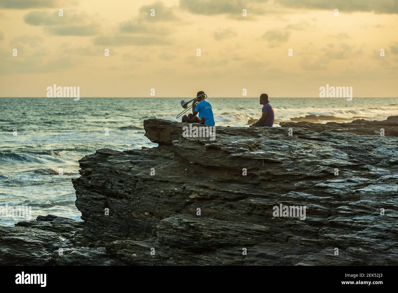 Sitzen und Posaune spielen auf den Felsen bei der Meer entlang der Accra Küste in Ghana Westafrika 2020 November 9 Stockfoto
