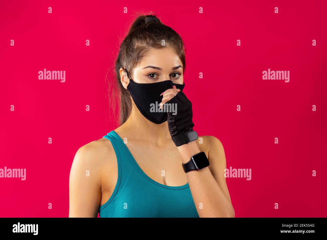 Portrait der kaukasischen Fitnessfrau in Sportbekleidung und medizinischer Schutzmaske mit Sporthandschuhen, Indoor-Studio, roter Hintergrund. Fitnesskurse während Stockfoto