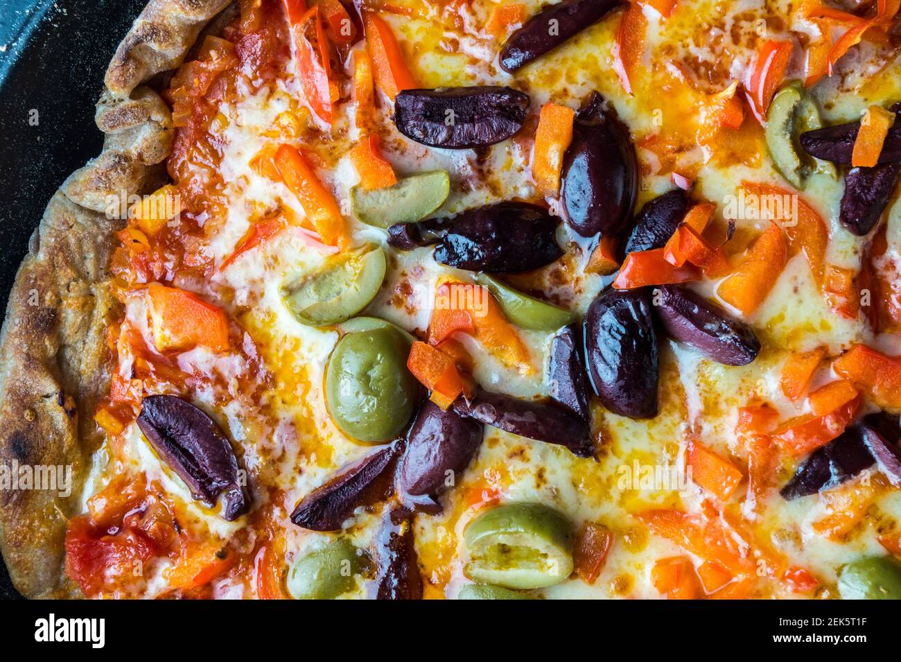 Nahaufnahme einer gegrillten hausgemachten Pizza mit Tomatenmark, Chorizo, Olive, Cheddar-Käse und Paprika Belag in einer blauen Le Creuset Bratpfanne Stockfoto