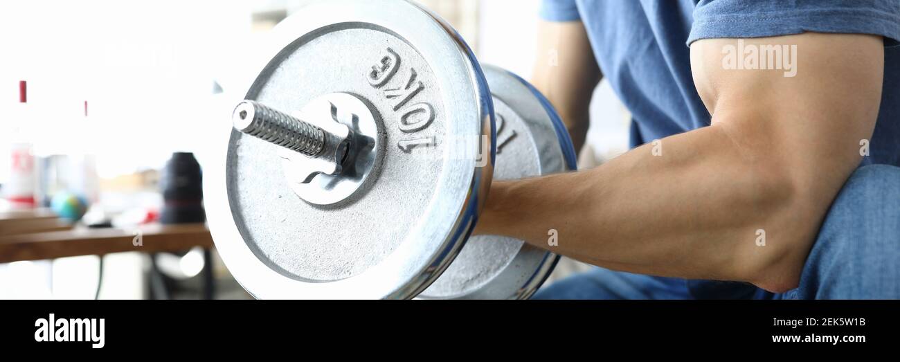 Mann sitzt auf Simulator und pumpt Muskeln mit schweren Gewichten. Stockfoto