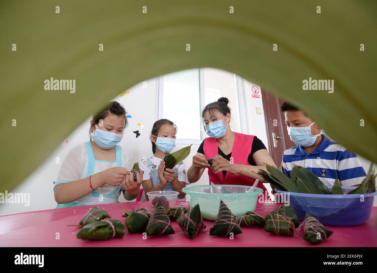 Nach einer freiwilligen Helferin lernen Jugendliche vor dem Drachenbootfest in Handan, der nordchinesischen Provinz Hebei, Zongzi, traditionelles chinesisches Reisgericht aus klejezem Reis, gefüllt mit verschiedenen Füllungen und in Bambusblätter verpackt, zu machen. Der 23. Juni 2020. Stockfoto