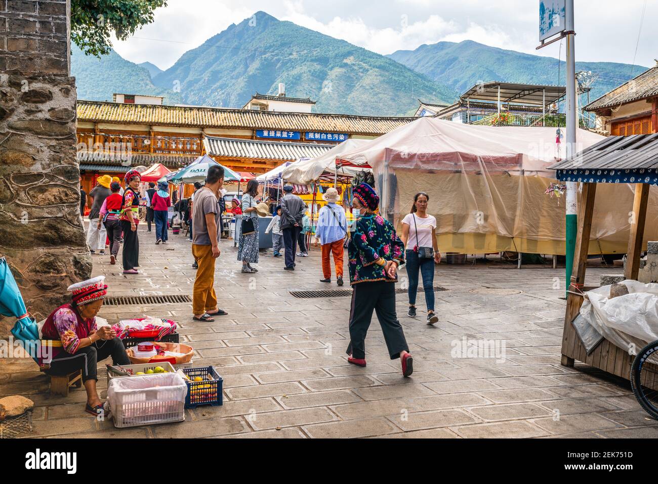 Dali China , 6. Oktober 2020 : Zhoucheng Dorf Marktplatz Ansicht mit Bai Minderheit Menschen in traditioneller Kleidung und Cangshan Berg im Hintergrund Stockfoto