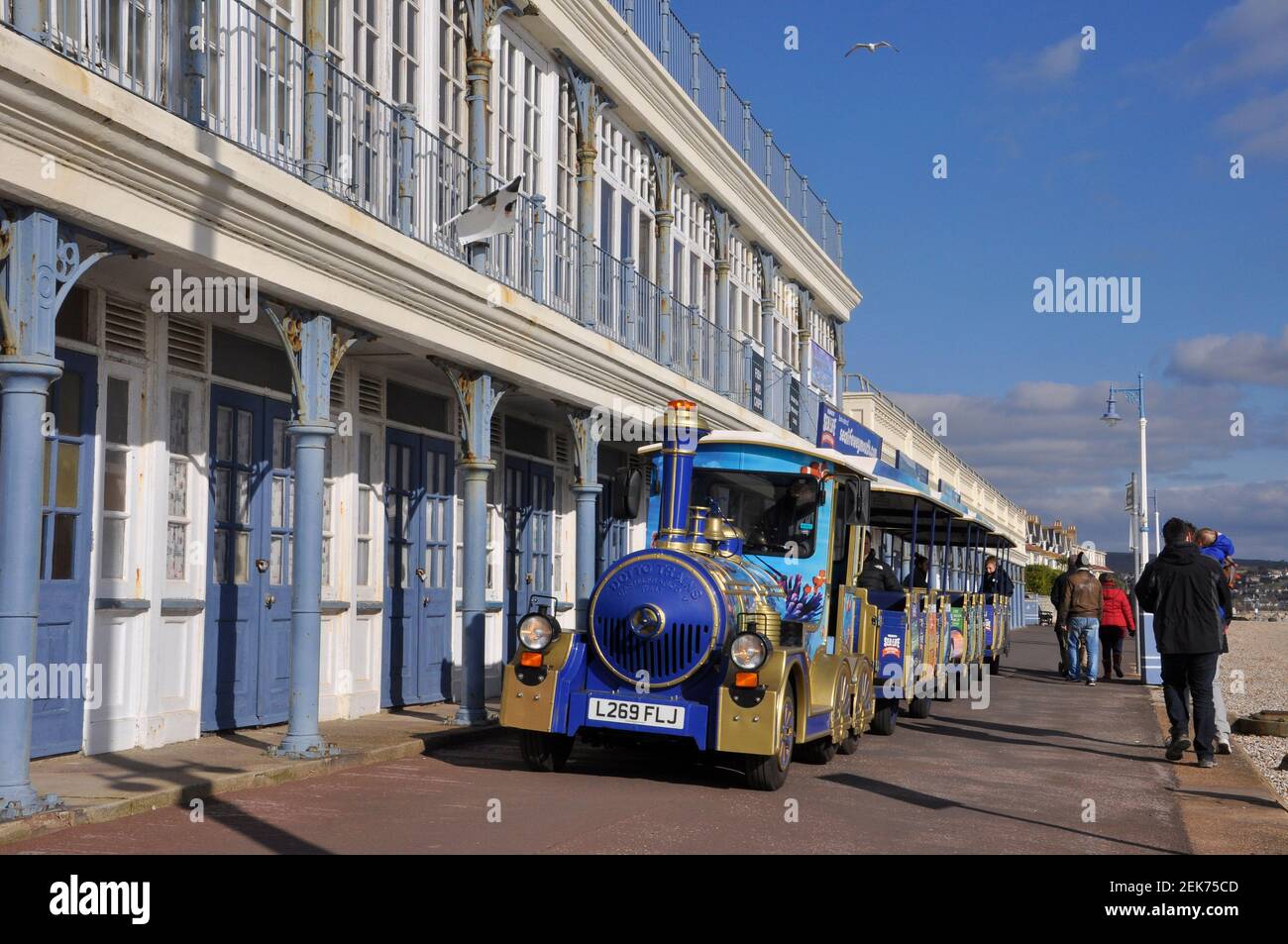 Der Landzug in Weymouth fährt entlang der Promenade vor den viktorianischen Umkleidekabinen. Stockfoto