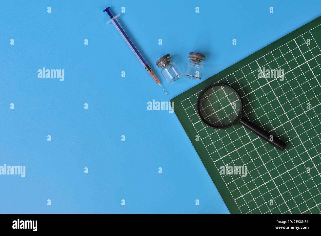 Layout von Graph Pad, Glasfläschchen, Spritze und Lupe mit leerem Platz für Text auf blauem Hintergrund Stockfoto