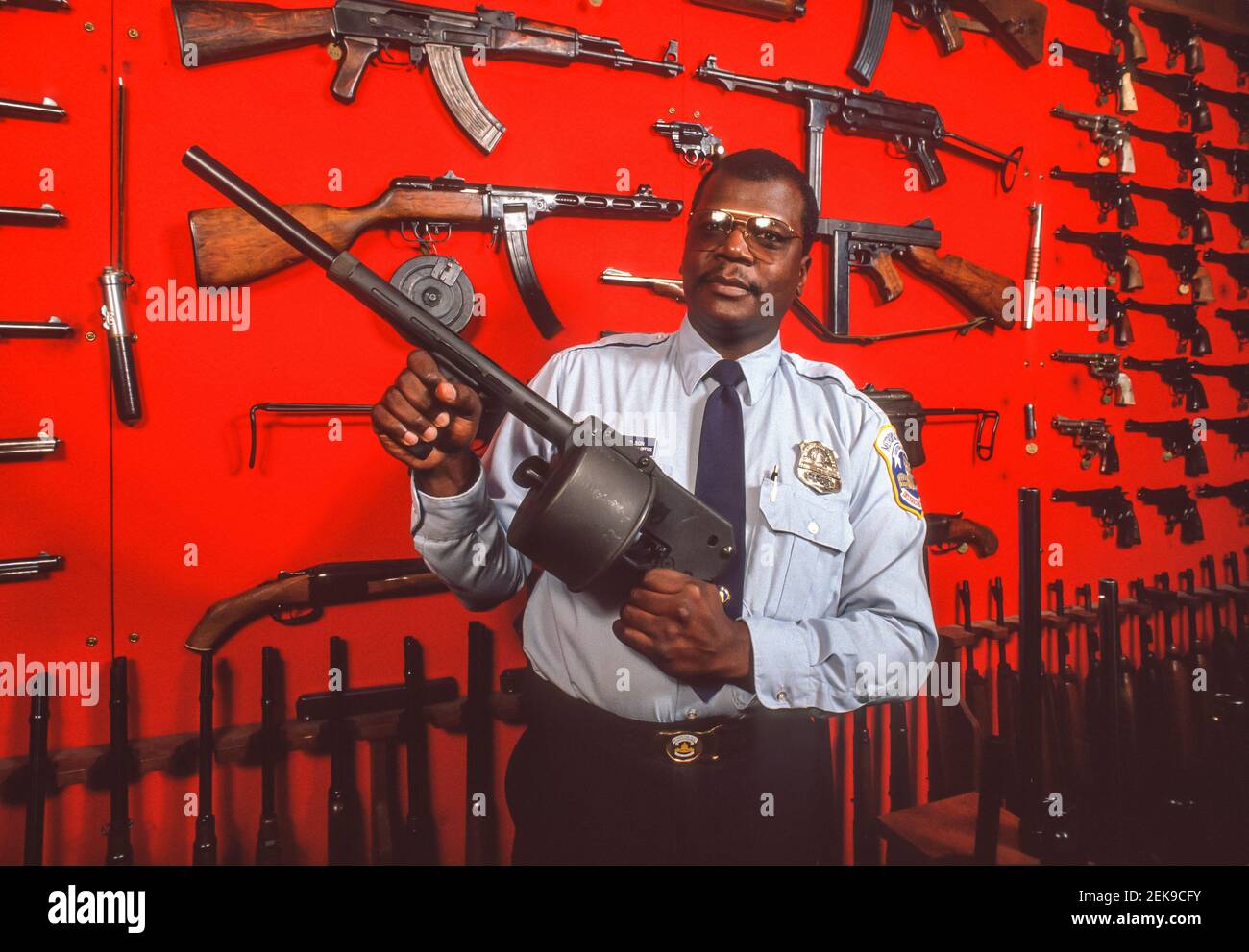 WASHINGTON, DC, USA - Polizeibeamter hält die Waffe vor der Ausstellung beschlagnahmter Waffen, die von DC's Metropolitan Police Department, MPD, auf den Straßen beschlagnahmt wurden. Stockfoto