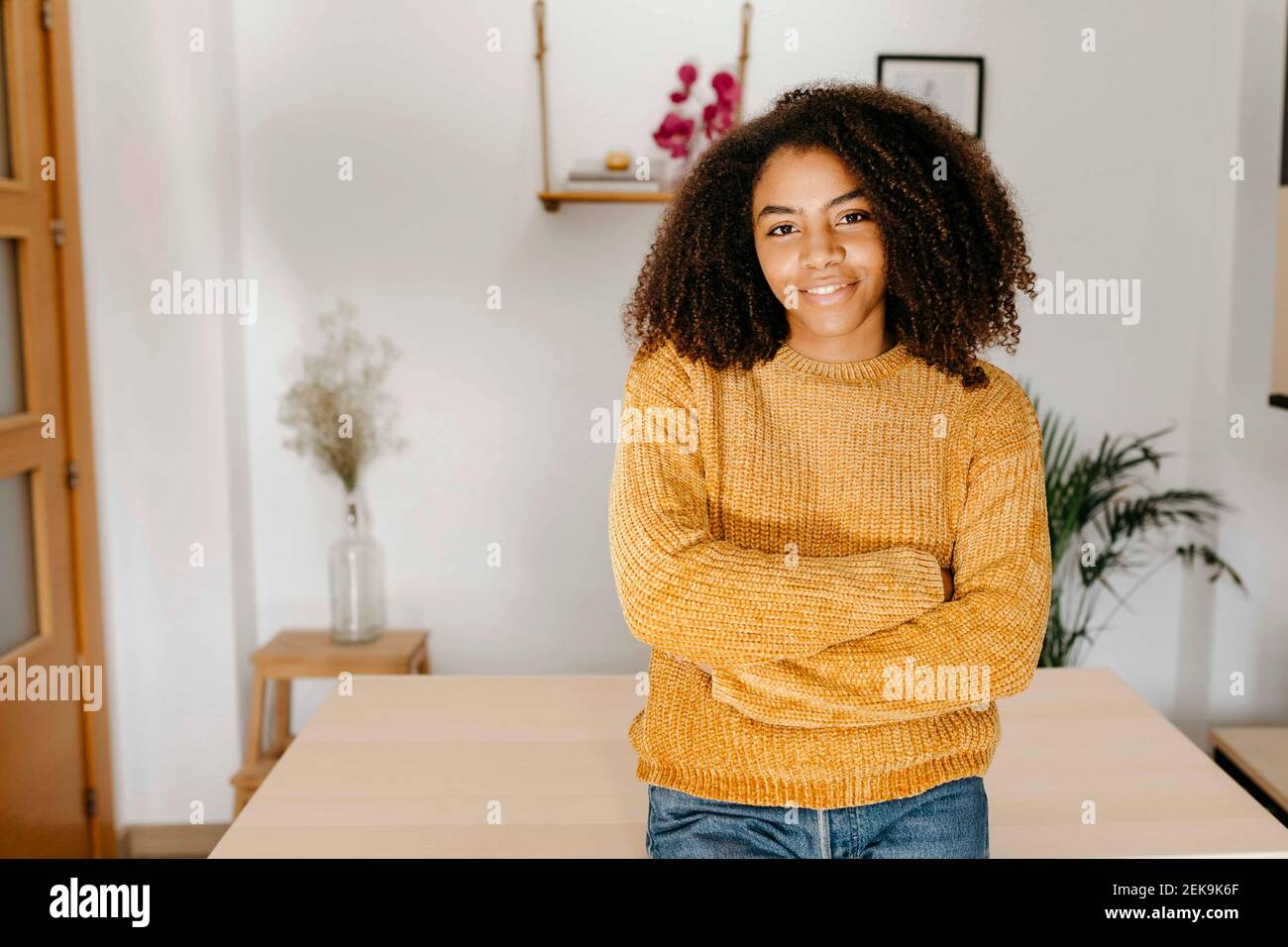 Frau mit lockigen Haaren, die zu Hause mit gekreuzten Armen steht Stockfoto